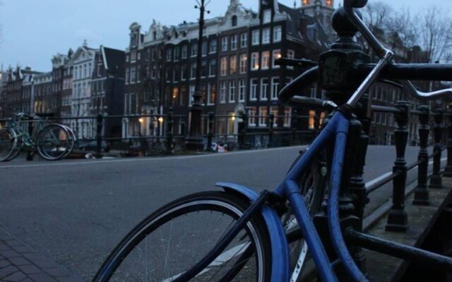 Un bicicletta blu in primo piano e, sullo sfondo, i palazzi di Amsterdam